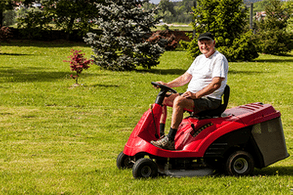 Senior man driving a red lawn mower (tractor) and looking towards the camera