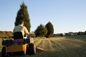 Middle aged man on zero turn mower cutting grass on a sunny day with the sun low in the sky